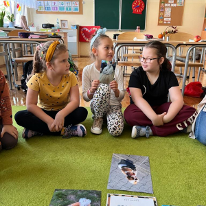 Dzień zwierząt w klasie pierwszej - uczniowie siedzą na dywanie i oglądają zdjęcia swoich pupili.